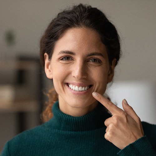 Woman in sweater pointing to her smile